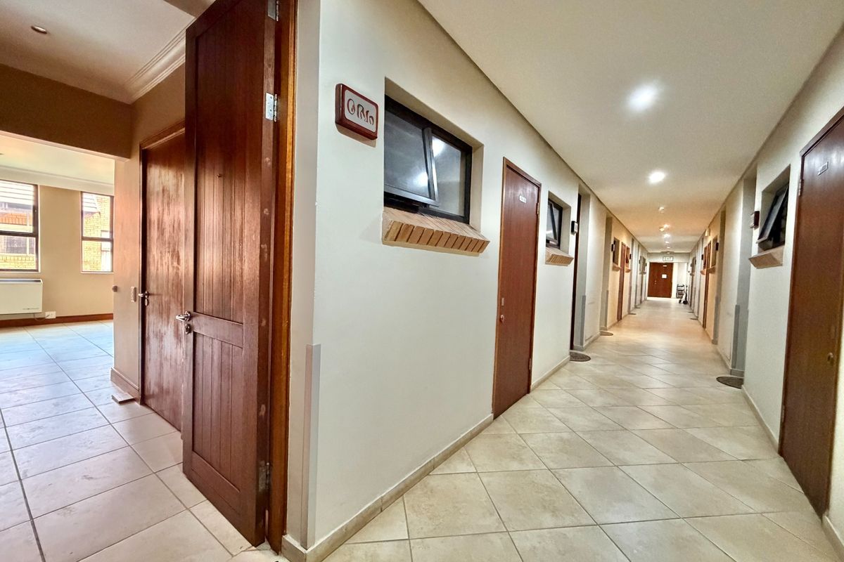 A long, well-lit interior hallway featuring tiled flooring, multiple timber doors, and small awning windows along the wall.