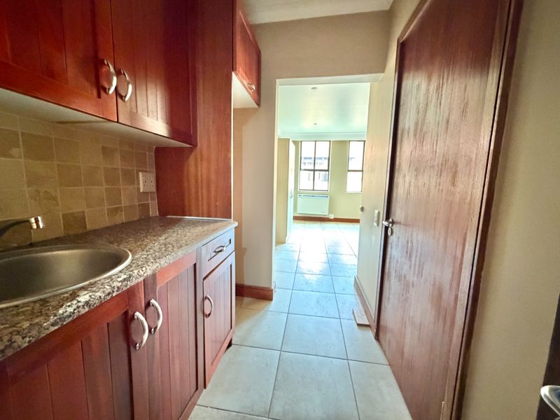 A functional scullery area featuring built-in wooden cabinetry, granite countertops, and a stainless steel sink, leading through to an open-plan living space.