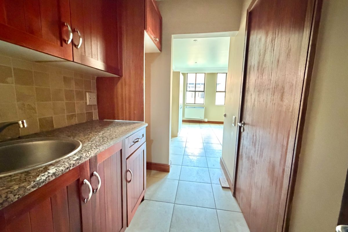A functional scullery area featuring built-in wooden cabinetry, granite countertops, and a stainless steel sink, leading through to an open-plan living space.