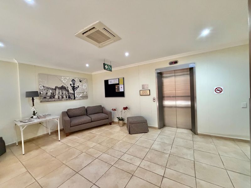 A clean and functional building lobby or hallway featuring tiled flooring, a stainless steel elevator, and integrated ceiling air conditioning.