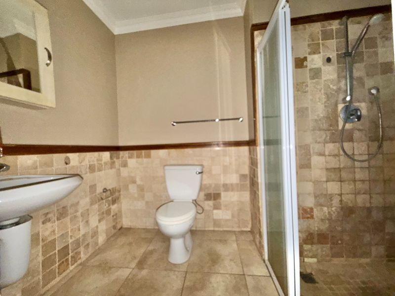 A functional bathroom featuring a pedestal basin, toilet, and a shower enclosure with tiled walls and flooring throughout.