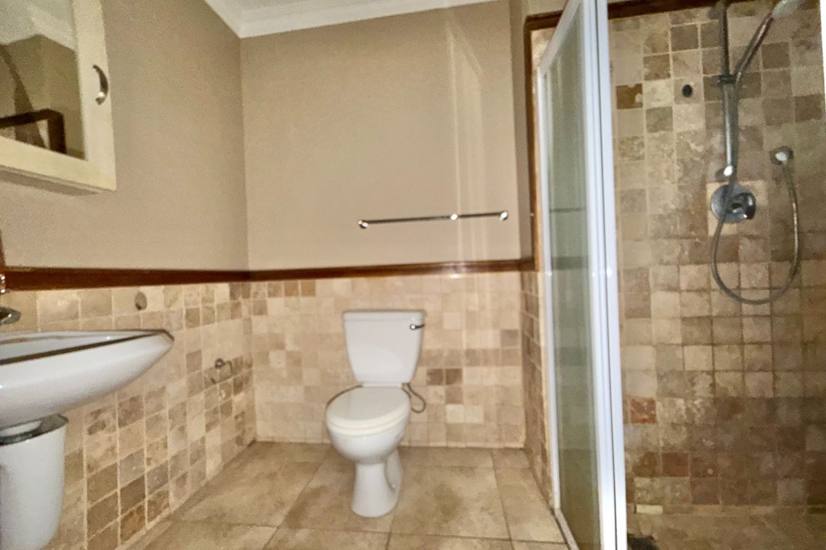 A functional bathroom featuring a pedestal basin, toilet, and a shower enclosure with tiled walls and flooring throughout.