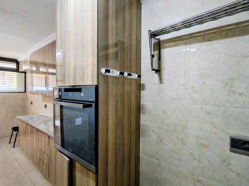 Modern kitchen featuring wood-finish cabinetry, built-in oven, granite countertops, and neutral tiled walls in a clean, well-maintained space.