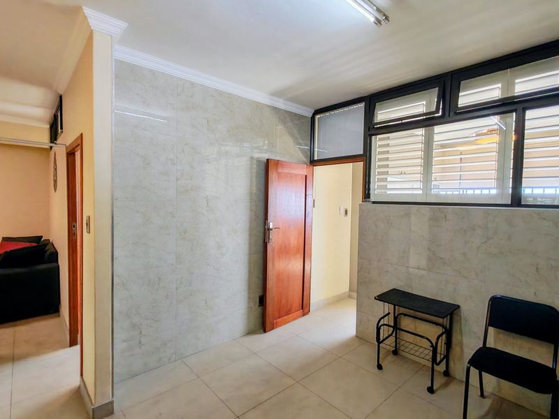 A bright, tiled hallway featuring marble-effect wall tiles, timber doors, and louvre windows, providing a clean and functional transition space within the apartment.