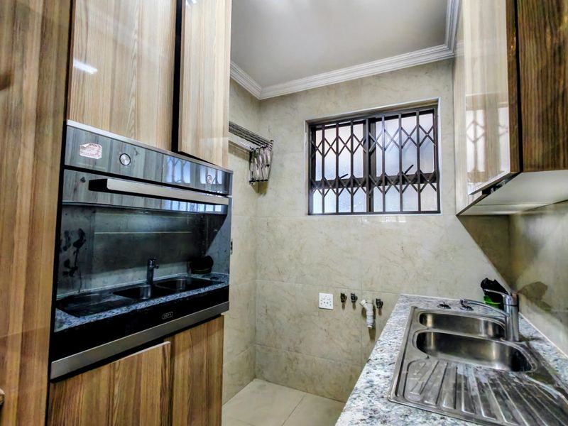 A functional scullery featuring built-in cabinetry, granite countertops, a double stainless steel sink, and a built-in oven with dedicated plumbing connections.