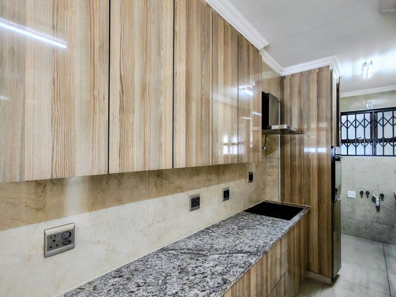 Modern kitchen featuring high-gloss wood-look cabinetry, granite countertops, integrated hob, extractor fan, and neutral tiled finishes throughout.