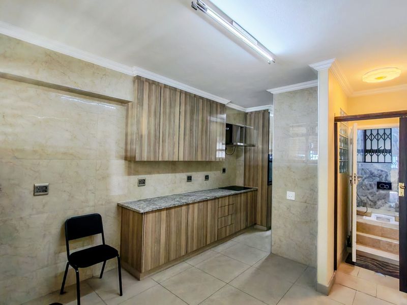 A modern kitchen featuring wood-finish cabinetry, granite countertops, integrated hob, and extractor fan, complemented by neutral wall tiling and tiled flooring.