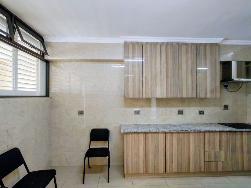 A clean, modern kitchen featuring wood-look laminate cabinetry, granite countertops, a built-in hob, and an extractor fan, finished with neutral wall and floor tiles.