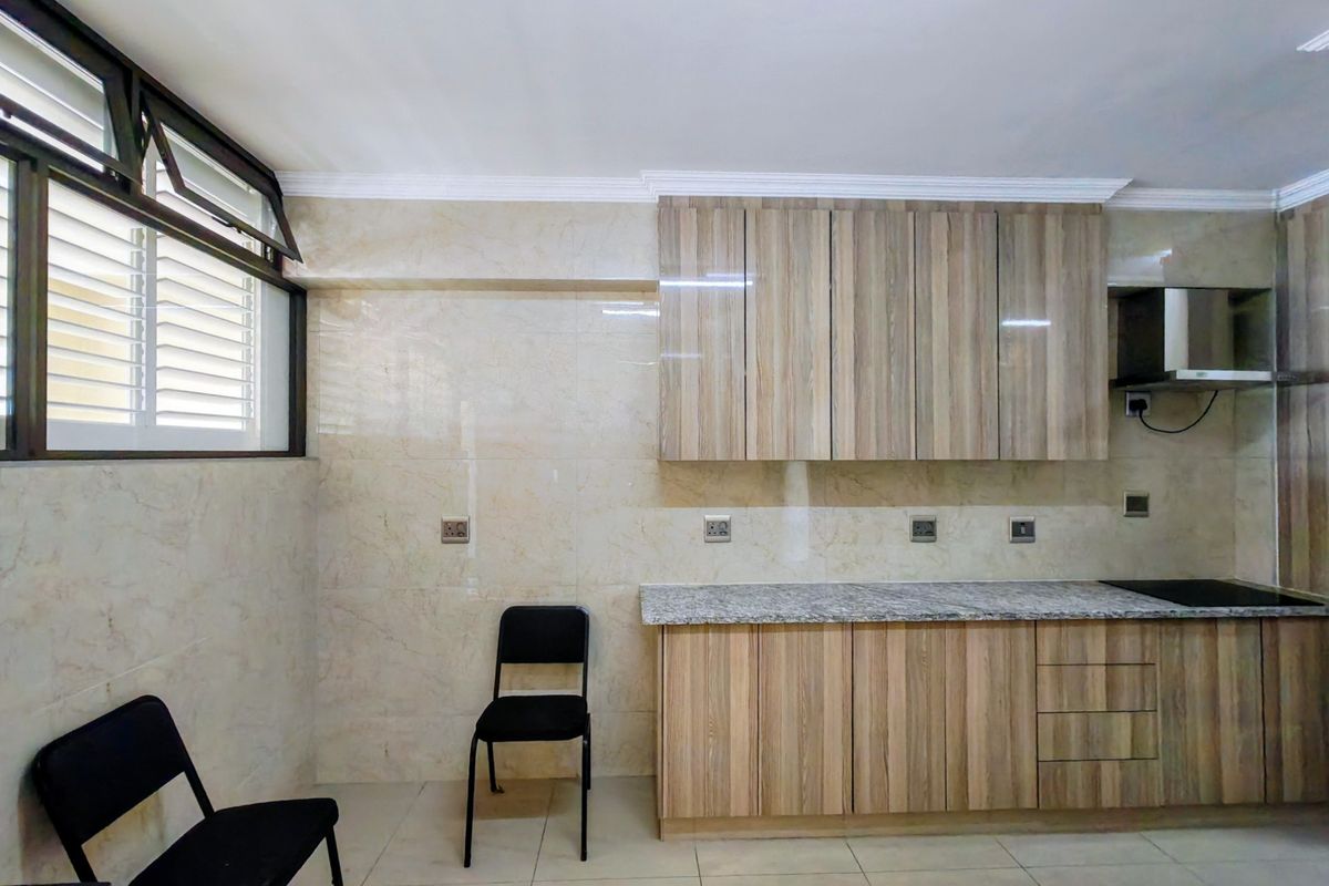 A clean, modern kitchen featuring wood-look laminate cabinetry, granite countertops, a built-in hob, and an extractor fan, finished with neutral wall and floor tiles.