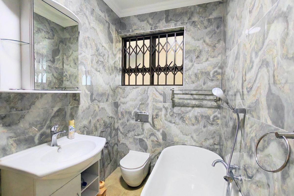 Modern bathroom featuring marble-effect wall tiling, a freestanding bathtub, wall-mounted vanity, and a secure window with a metal security gate.