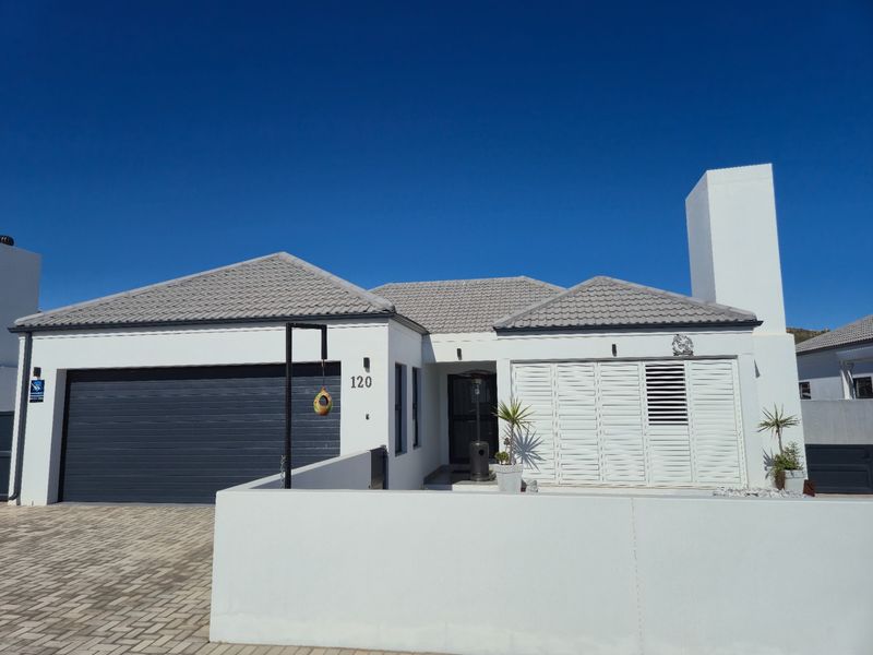A well-maintained single-story residential home featuring a double garage, tiled roof, and secure boundary wall with a paved driveway.