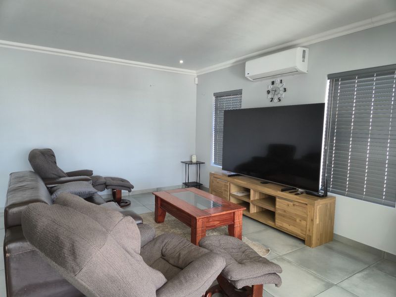 A comfortable living room featuring tiled flooring, cove cornicing, and a wall-mounted air conditioning unit with venetian blinds on the windows.