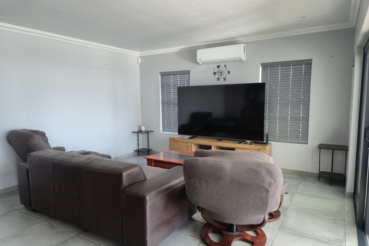 A spacious living room featuring tiled flooring, wall-mounted air conditioning, and venetian blinds, providing a comfortable and functional living space.