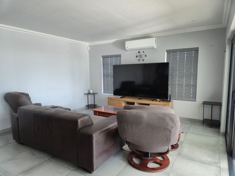 A spacious living room featuring tiled flooring, wall-mounted air conditioning, and venetian blinds, providing a comfortable and functional living space.
