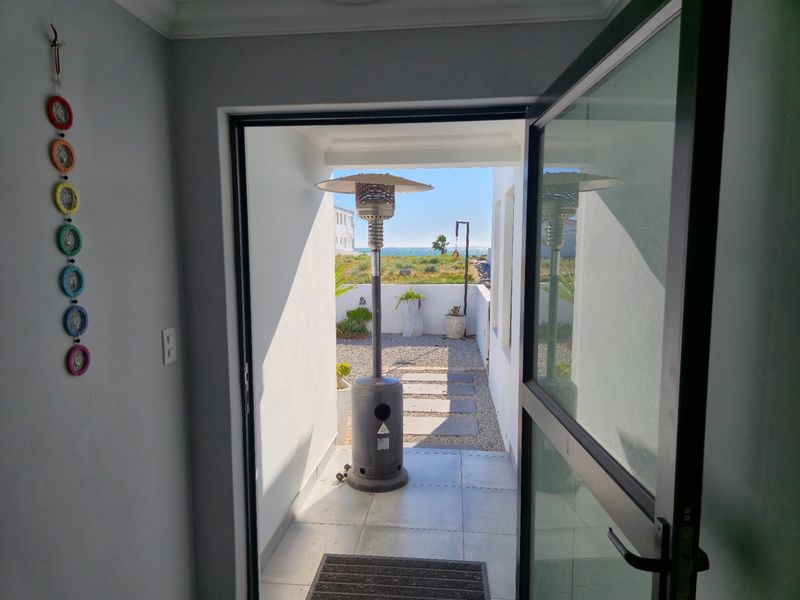A view from an interior doorway looking out onto a tiled patio area with stone paving leading towards a coastal garden setting.