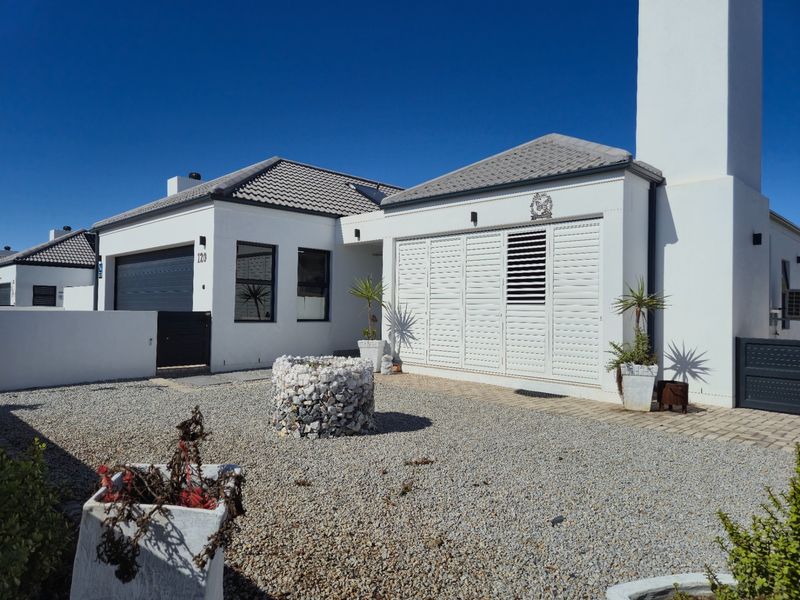 Modern single-story residence featuring a clean white facade, tiled roof, integrated garage, and secure shuttered windows set within a low-maintenance gravel garden.