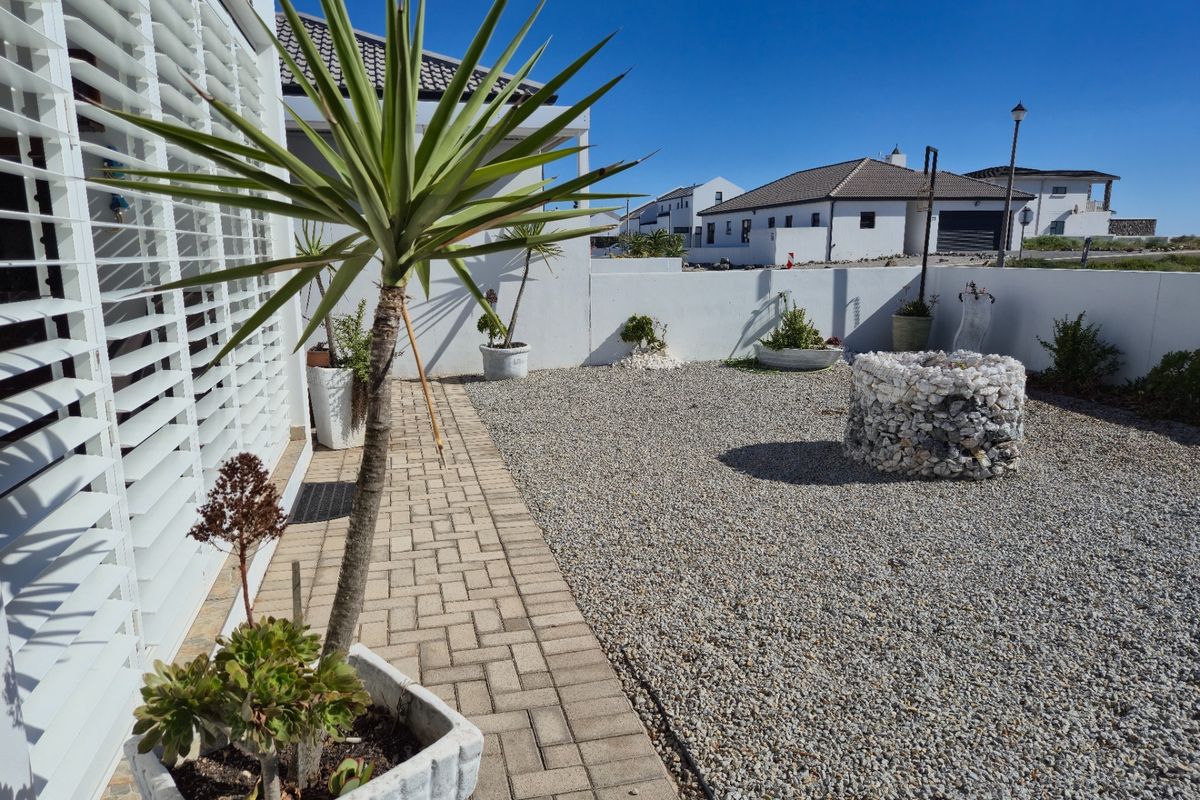 A low-maintenance rear courtyard featuring a paved walkway, gravel ground cover, and a decorative stone feature enclosed by a perimeter wall.