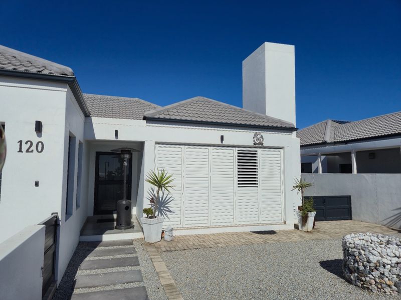 A well-maintained front facade featuring a modern white exterior, tiled roof, chimney stack, and secure shuttered doors with a neat gravel and paved entrance.