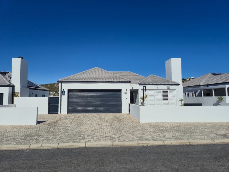 Modern single-story residential home featuring a paved driveway, double garage, and clean white exterior finishes under a tiled roof.