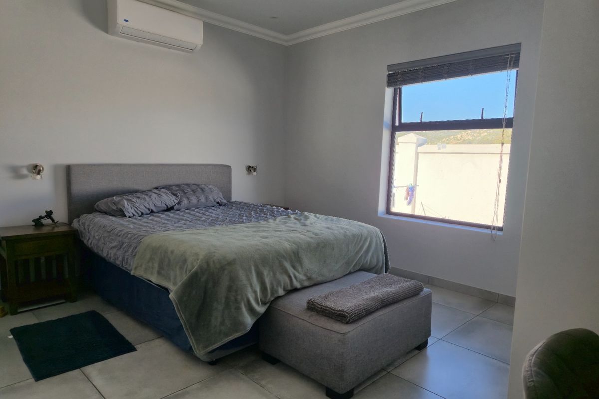 A well-maintained bedroom featuring neutral tiled flooring, a wall-mounted split-system air conditioner, and a window providing natural light.