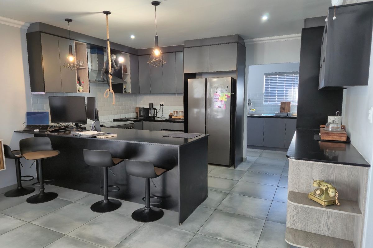 Modern open-plan kitchen featuring dark cabinetry, a central island with breakfast bar seating, stone countertops, and a separate scullery area.