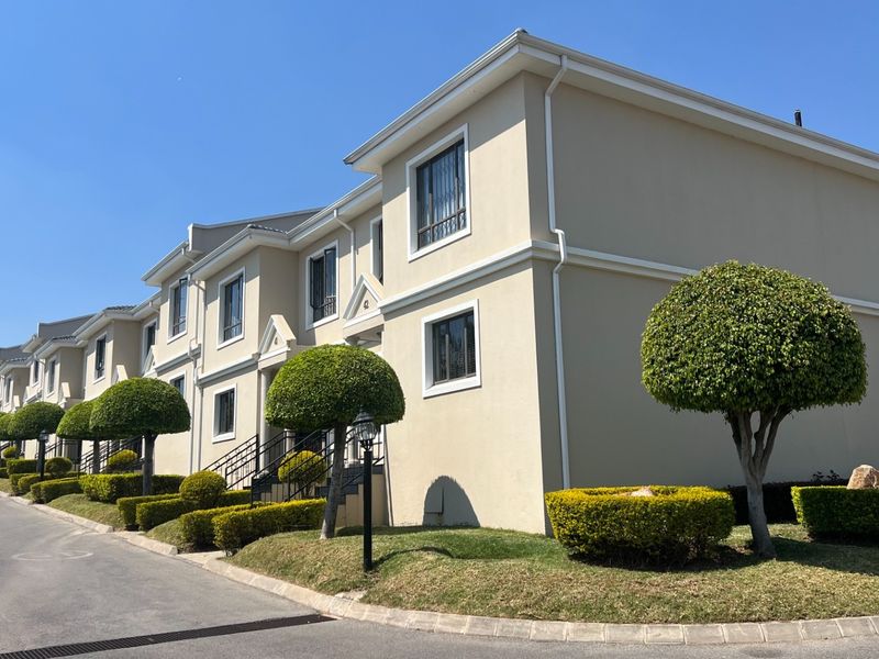 A well-maintained townhouse complex featuring a clean stucco facade, manicured hedges, and paved driveway access.