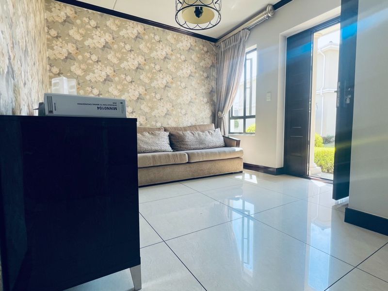 A bright living room featuring large format floor tiles, decorative floral wallpaper, crown molding, and direct access to the exterior through a glass-paneled door.