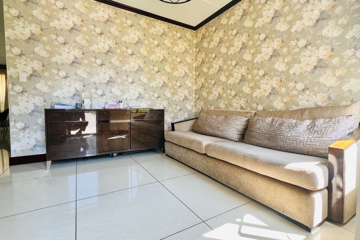 A living room featuring large format floor tiles, decorative floral wallpaper, and crown molding, offering a neutral base for interior updates.