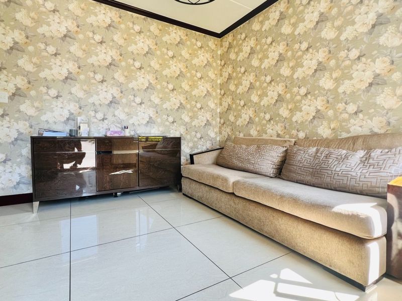 A living room featuring large format floor tiles, decorative floral wallpaper, and crown molding, offering a neutral base for interior updates.