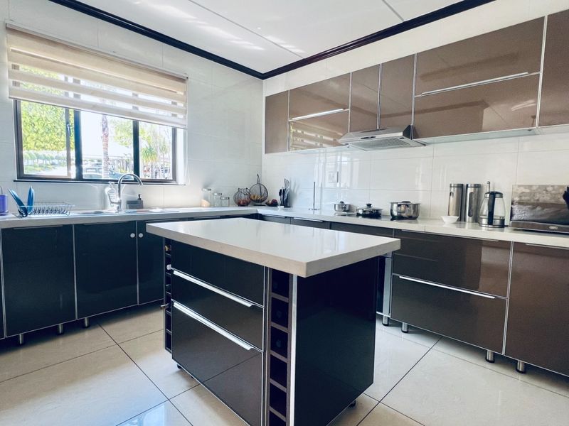 Modern kitchen featuring high-gloss cabinetry, a central island with stone countertops, tiled flooring, and a functional layout with integrated extractor fan.