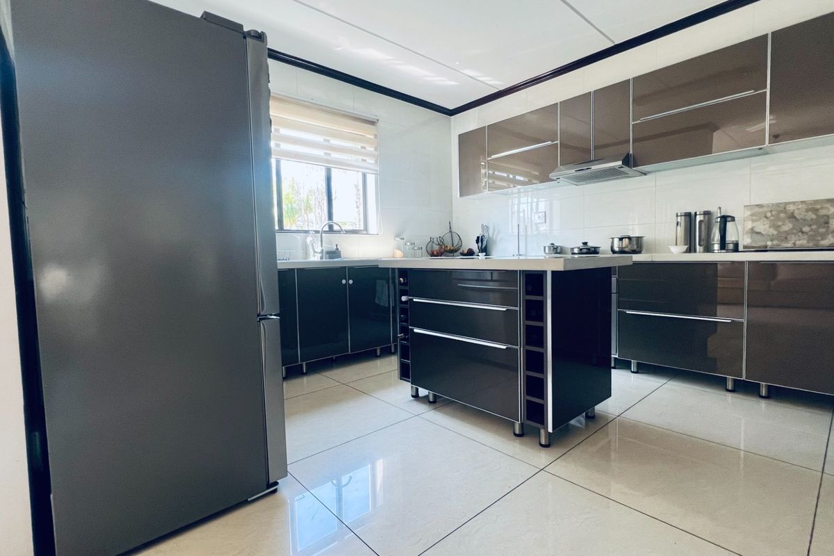 Modern kitchen featuring high-gloss cabinetry, a central island, tiled flooring, and a functional layout with integrated extractor fan and sink.