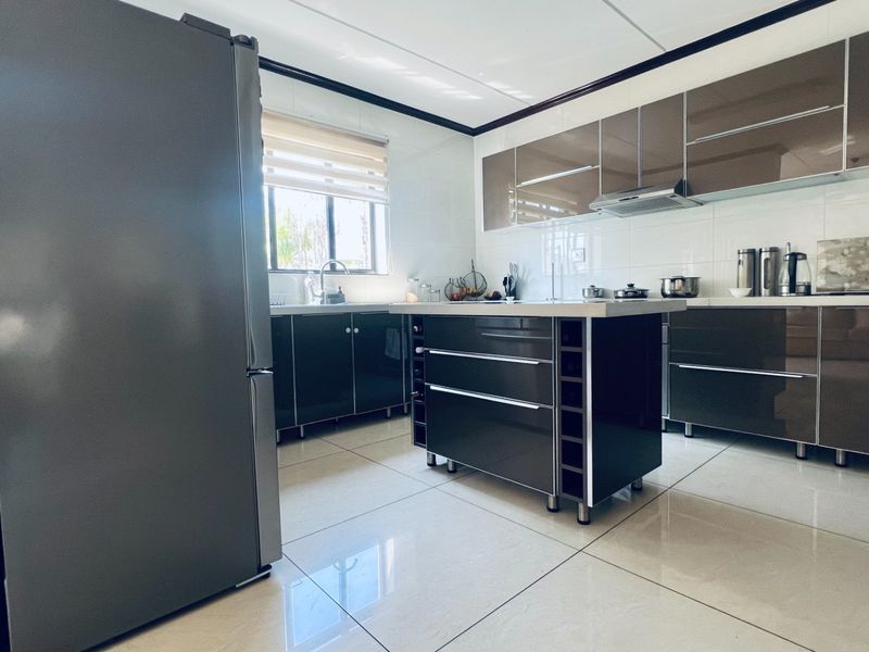 Modern kitchen featuring high-gloss cabinetry, a central island, tiled flooring, and a functional layout with integrated extractor fan and sink.