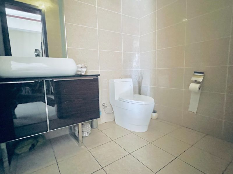 A functional bathroom featuring a modern vanity with a vessel sink, wall-mounted mirror, and neutral ceramic tiling throughout.