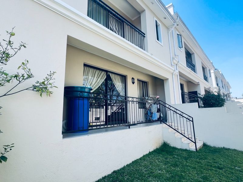 Rear elevation of a townhouse featuring a tiled patio, wrought iron railings, and sliding glass door access to the ground floor living area.