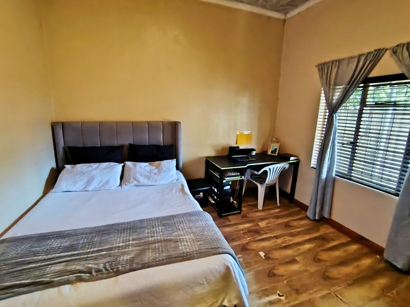 A bedroom featuring laminate flooring, window blinds, and neutral wall tones, currently showing signs of wear on the floor and ceiling.