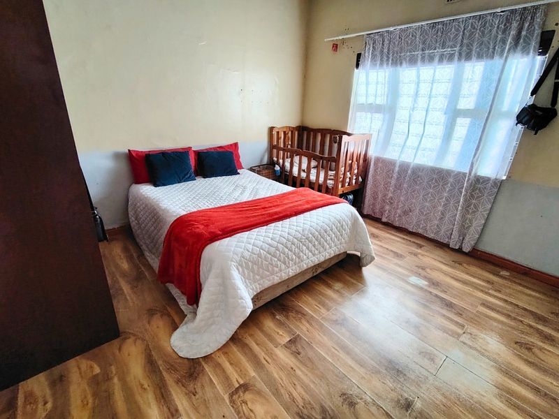 A bedroom featuring laminate flooring and a window with a curtain rail, requiring cosmetic updates to the wall finishes.