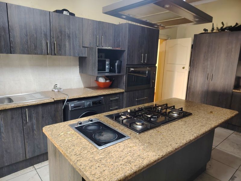 Kitchen featuring dark wood cabinetry, granite countertops, dual hobs, built-in oven, and an overhead extractor fan.
