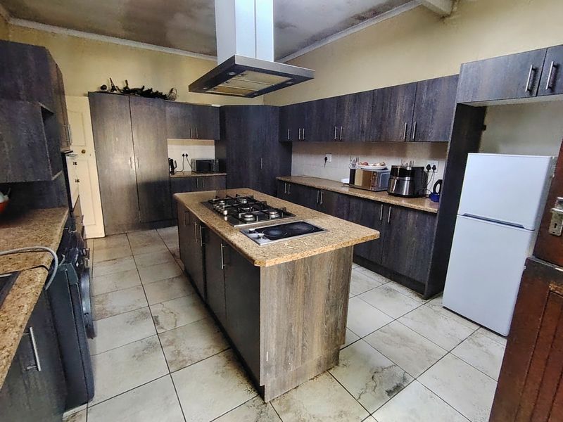 Spacious kitchen featuring dark wood cabinetry, a central island with dual hobs, granite countertops, and tiled flooring, requiring some cosmetic updates.