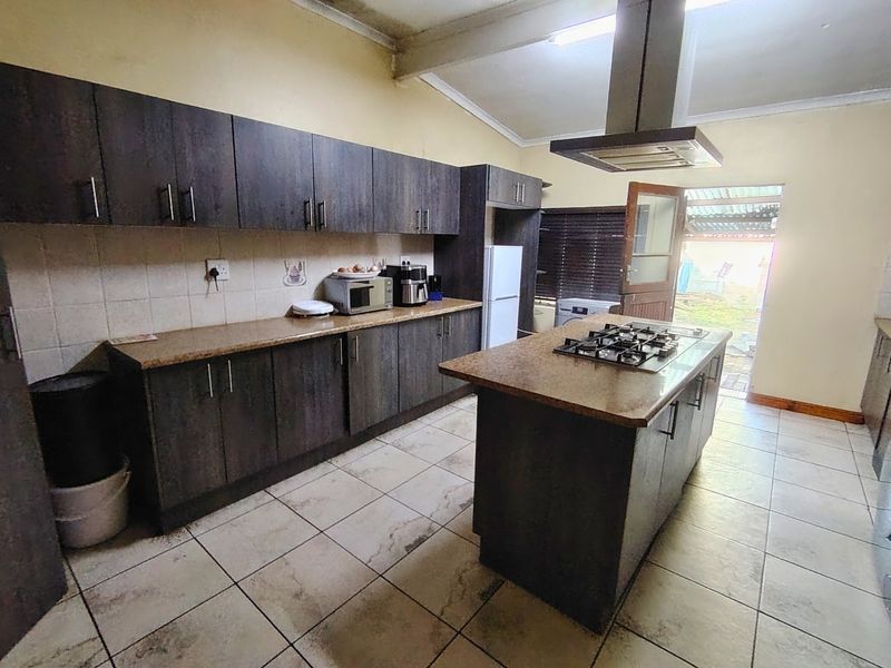 Kitchen featuring dark wood cabinetry, a central island with a gas hob, extractor fan, and tiled flooring with direct access to the rear exterior.