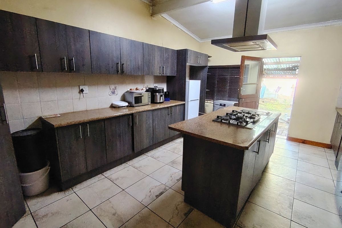Kitchen featuring dark wood cabinetry, a central island with a gas hob, extractor fan, and tiled flooring with direct access to the rear exterior.
