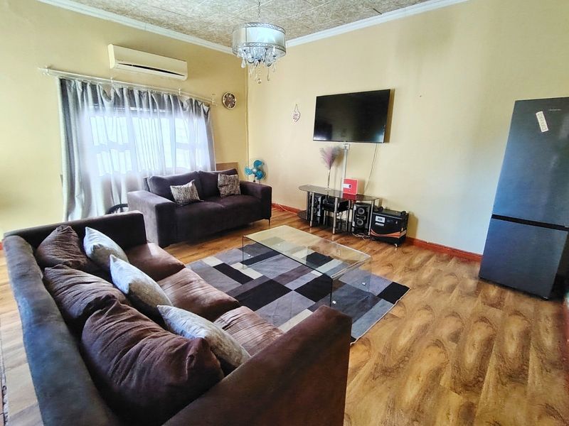 A living room featuring laminate flooring, a wall-mounted air conditioning unit, and textured ceiling tiles.