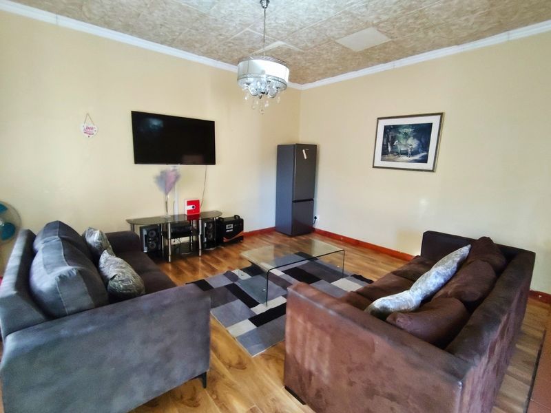 A living room featuring laminate flooring and a coved ceiling with a central pendant light fixture.