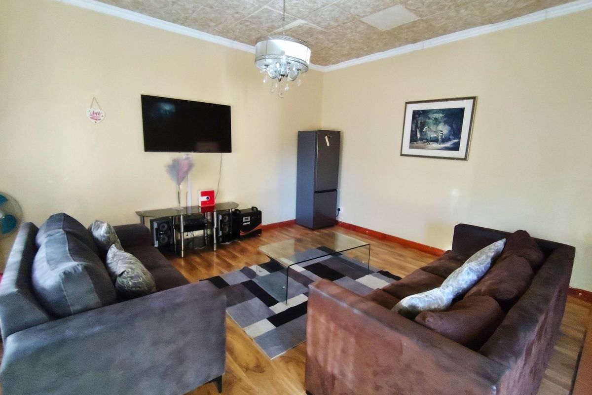 A living room featuring laminate flooring and a coved ceiling with a central pendant light fixture.