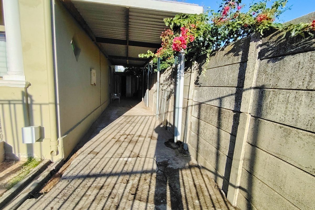 A narrow side passage featuring a concrete boundary wall, paved flooring, and a covered roof structure.