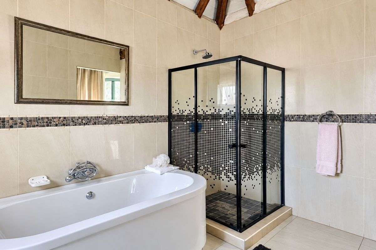 A well-maintained bathroom featuring a modern freestanding bathtub, a corner shower enclosure with decorative tiling, and exposed timber ceiling beams.