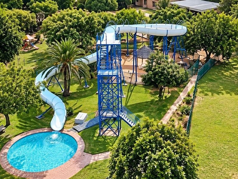 Aerial view of a recreational pool area featuring a large water slide, circular swimming pool, and landscaped garden surroundings.