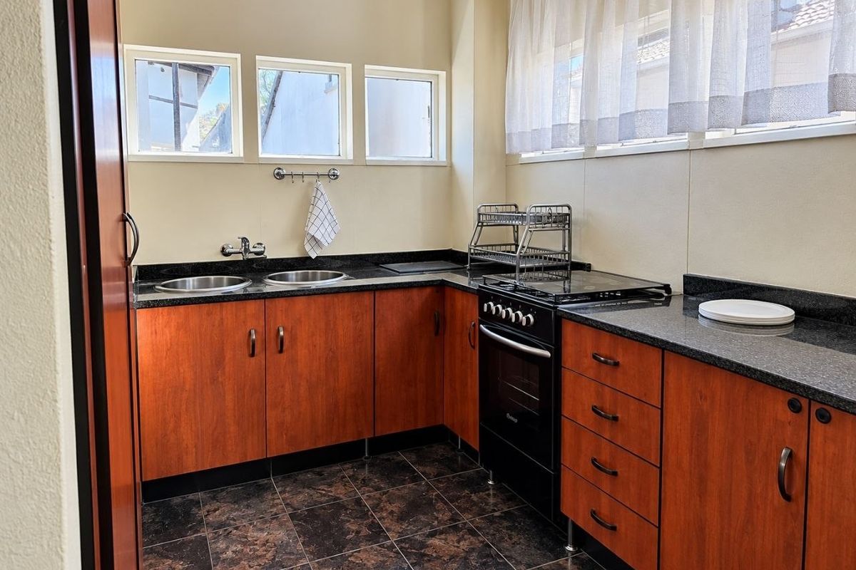 A functional kitchen featuring dark granite countertops, wood-finish cabinetry, a freestanding oven, and a double sink with tiled flooring.