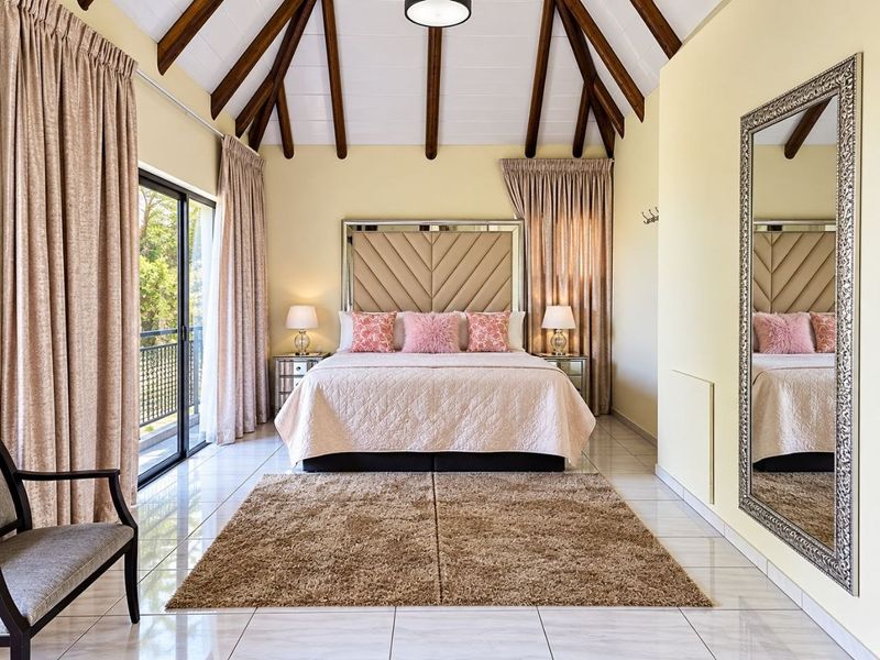 Spacious bedroom featuring a high vaulted ceiling with exposed timber rafters, tiled flooring, and direct access to a private balcony through sliding glass doors.