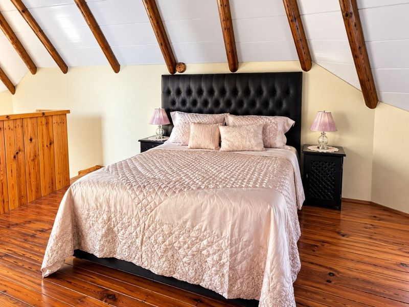 A cozy bedroom featuring exposed timber ceiling beams, warm timber flooring, and a wooden balustrade overlooking the lower level.