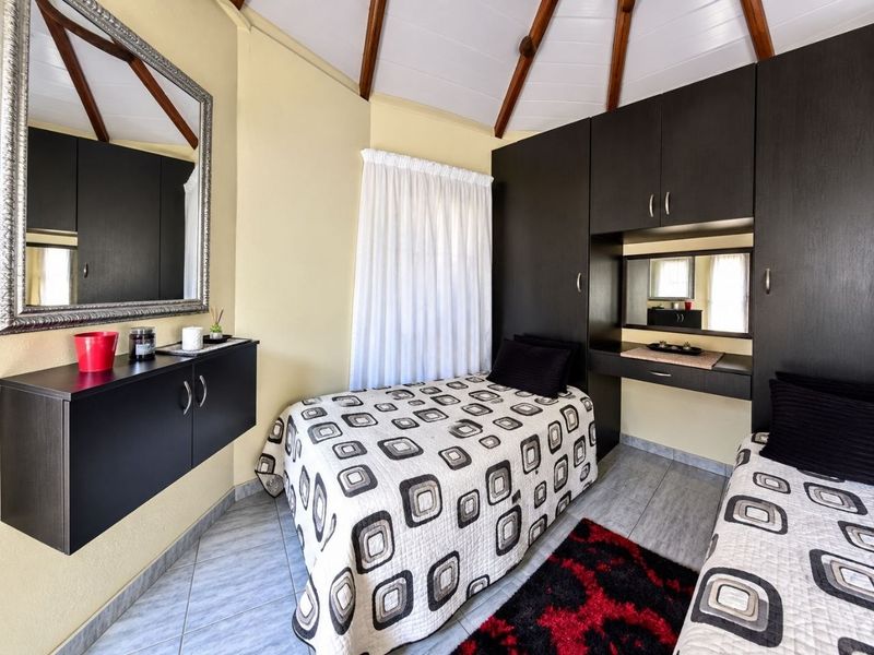 A compact bedroom featuring tiled flooring, a vaulted ceiling with exposed timber beams, and extensive built-in cabinetry with an integrated vanity unit.